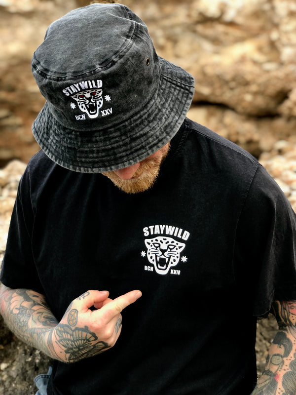 Person wearing the Stay Wild bucket hat and matching black t-shirt, both featuring the white panther logo and bold lettering