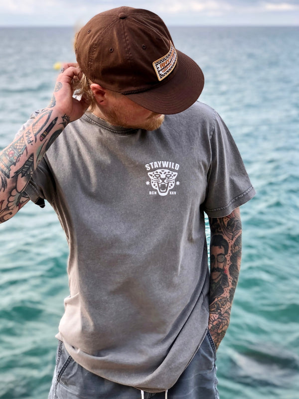 Person standing near the ocean wearing the Lost in the Wild t-shirt, showing the front logo with the Stay Wild panther