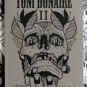 Close-up of the Sketchbook II cover by Toni Donaire, featuring a bold black ink skull illustration with symmetrical elements on a beige background.